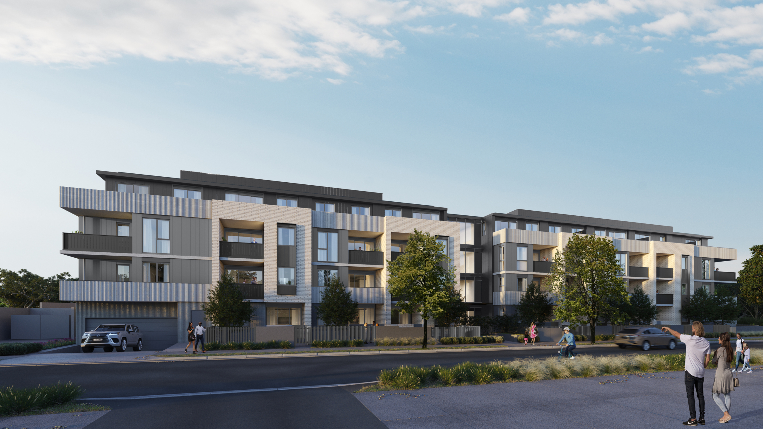 A modern four-story apartment building with balconies, large windows, and trees in front. People are walking on the sidewalk and a car is parked by the building under a clear sky.