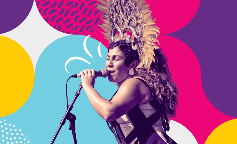 A woman wearing a large, ornate feathered headdress sings into a microphone, with a colorful abstract background of bold circles and patterns in pink, blue, yellow, and purple.
